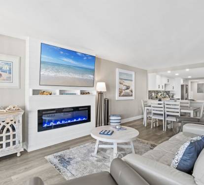 Relax in your sophisticated living area with coastal artwork, electric fireplace, and open kitchen perfect for memorable evenings together.