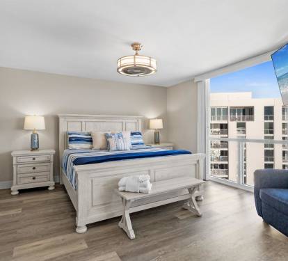 Your coastal-inspired bedroom awaits with crisp linens, ocean artwork, and a city view that frames your perfect beach getaway retreat.