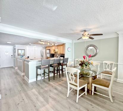 Your open-concept dining and kitchen space flows seamlessly with elegant white chairs, granite counters, and warm coastal colors.