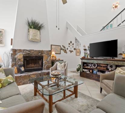 Unwind in your spacious living room where natural stone fireplace warmth meets modern comfort beneath soaring ceilings.