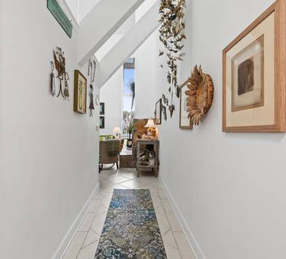 Step into your bright hallway adorned with curated artwork and tropical accents, leading you to comfortable living spaces filled with character.
