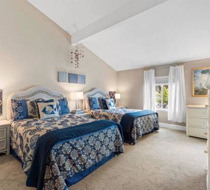 Relax in your charming twin bedroom featuring elegant blue and white linens, wicker furnishings, and artwork creating a coastal cottage feel.