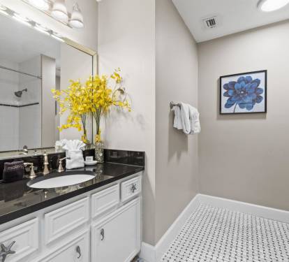 Step into your elegant bathroom featuring a marble-topped vanity, bright Hollywood-style lighting, and fresh blooms welcoming you home.