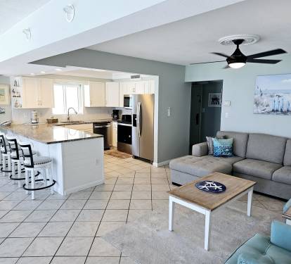 Relax in your spacious open-plan living space with fully-equipped kitchen, comfortable seating, and coastal-themed décor for the perfect beach getaway.