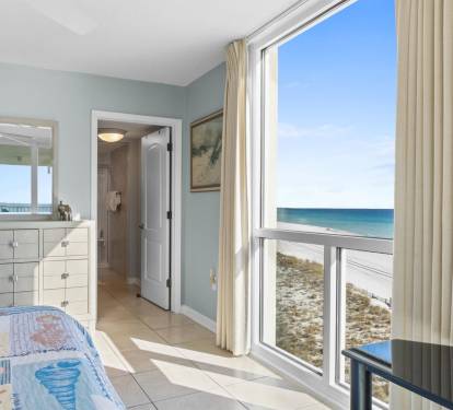 Wake up to stunning ocean views through floor-to-ceiling windows in this peaceful bedroom with soft coastal colors and direct beach access.