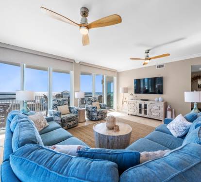 Unwind in your spacious living room where plush blue seating surrounds a rustic coffee table, while floor-to-ceiling windows frame stunning views.