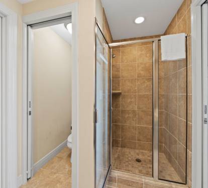 Step into your private spa-like shower featuring beautiful warm stone tile and sleek glass doors for the perfect refreshing escape.