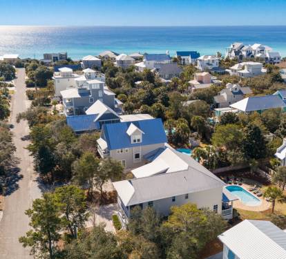Aerial view of a charming coastal neighborhood with vacation homes nestled among trees, just steps from pristine beaches.