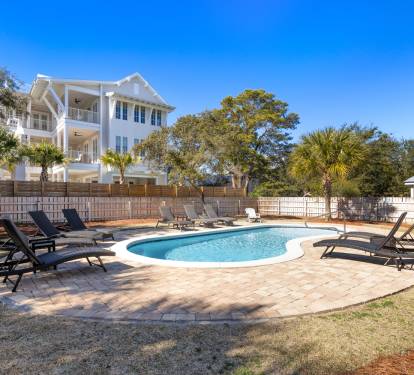 Private pool oasis with comfortable loungers surrounded by mature landscaping and stunning white coastal architecture.