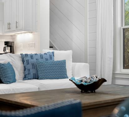 Sink into this cozy white sofa with plush blue pillows, where natural light streams through your windows as you unwind in style.