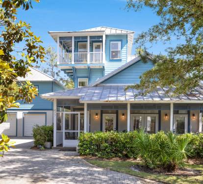 Charming coastal home with distinctive blue siding and metal roof, featuring wraparound porches and mature landscaping in a peaceful setting.