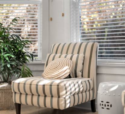 Settle into your private reading nook by bright windows, where natural light filters through blinds onto a comfy striped chair.