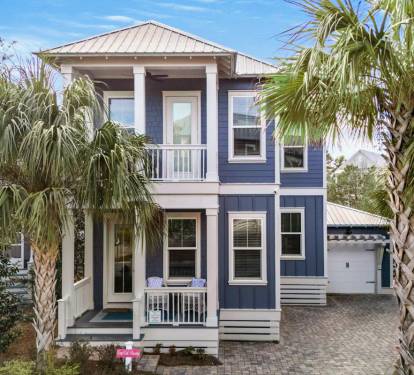 Charming coastal home with distinctive blue siding and white trim, surrounded by tropical palm trees and lush landscaping.