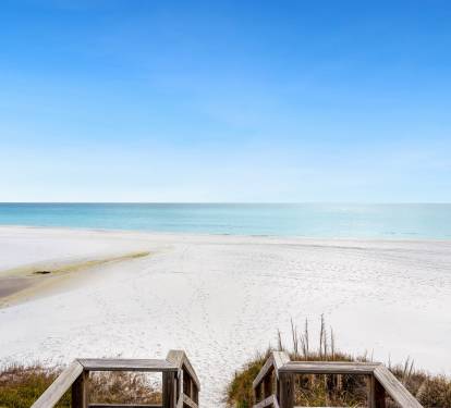 Pristine white sand beach meets crystal-clear turquoise waters under an endless blue sky, accessed by charming wooden walkway.