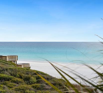 Pristine beach with crystal-clear turquoise waters and wooden boardwalk access through coastal vegetation.