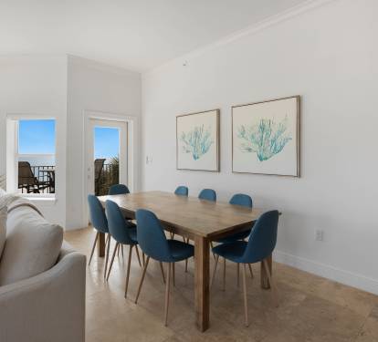 Your bright dining space opens to stunning gulf views through floor-to-ceiling windows, where coastal artwork complements the serene blue palette.