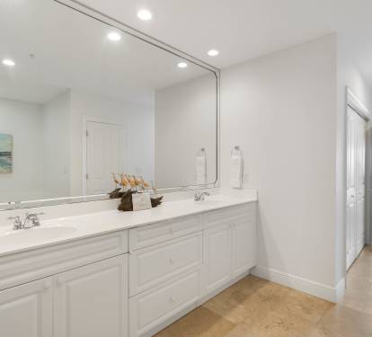 Your luxurious bathroom features dual vanities with pristine white cabinetry, elegant marble countertops, and a large mirror perfect for your morning routine.