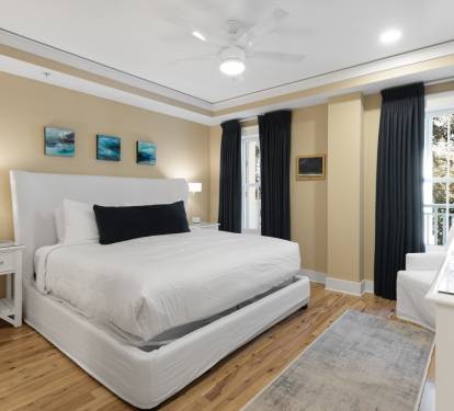 Unwind in your peaceful bedroom featuring a plush white bed, warm wood floors, and serene ocean artwork above your headboard.