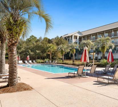 Sparkling pool surrounded by swaying palm trees and comfortable loungers under vibrant red umbrellas—your perfect spot to unwind.