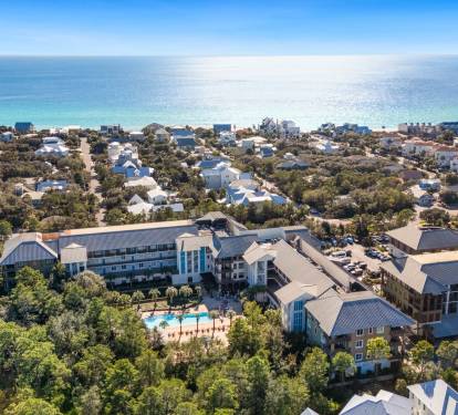 Aerial view of resort property nestled among coastal homes, featuring swimming pool and direct beach access.