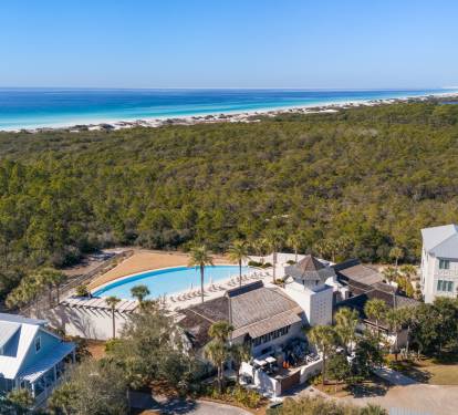 Stunning aerial view of vacation properties nestled between lush forest and pristine white sand beaches with crystal-clear turquoise waters.