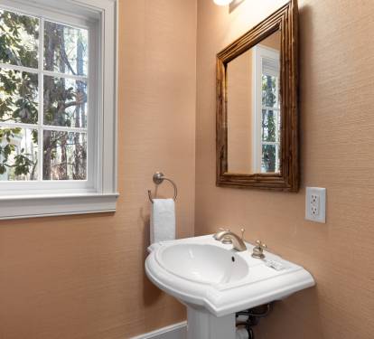 Freshen up in your elegant powder room featuring a classic pedestal sink, warm natural lighting, and charming garden views.