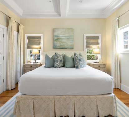 Drift into peaceful sleep on this plush bed, surrounded by warm coastal colors and soft natural light from French doors.