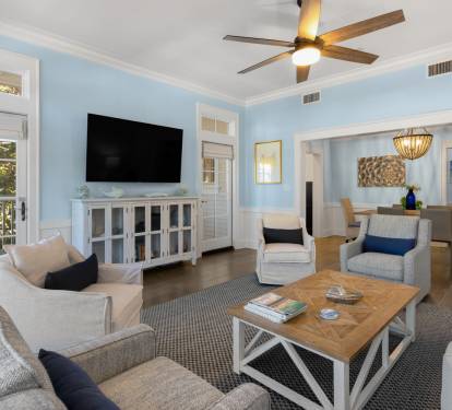 Relax in your stylish living room featuring cozy seating, a large TV, and gentle ceiling fan breeze flowing through French doors.