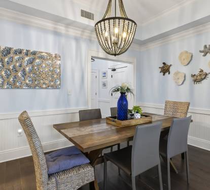 Gather around your elegant dining table beneath the stunning chandelier, where coastal artwork and warm nautical touches create the perfect atmosphere for memorable meals together.