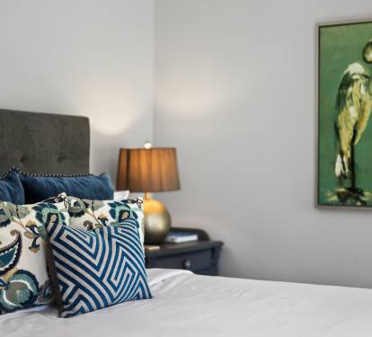 Sink into plush pillows and crisp linens in your serene retreat, where coastal artwork and warm lighting create the perfect atmosphere for restful nights.