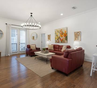 Gather with friends in your stylish living room featuring rich burgundy leather seating, warm hardwood floors, and elegant lighting.