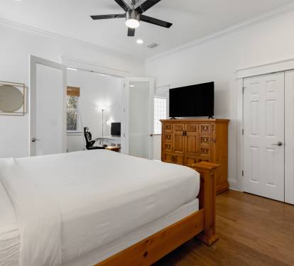 Unwind in your serene bedroom featuring crisp white linens, warm wood floors, and thoughtful touches like a ceiling fan for comfort.