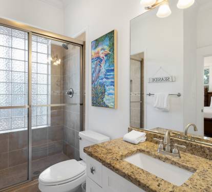 Your private bathroom features a spacious glass shower, granite countertops, and bright coastal artwork that adds charm to your daily routine.