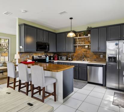 Your spacious kitchen features sleek navy cabinets, gleaming stainless appliances, and a warm brick backsplash, perfect for cooking memorable meals together.