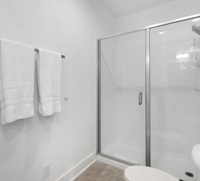 Step into your pristine bathroom featuring a spacious glass-enclosed shower with modern fixtures and fresh towels awaiting your arrival.