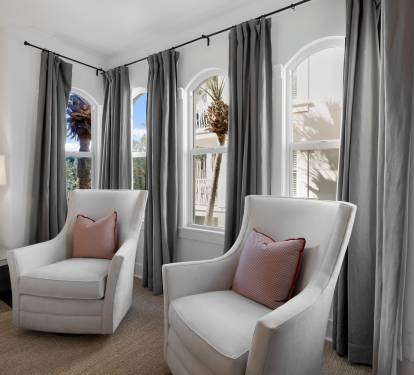 Sink into plush armchairs by graceful arched windows, where soft gray curtains frame palm-dotted views and morning light creates your perfect reading retreat.