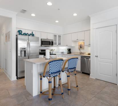 Your coastal-inspired kitchen awaits with crisp white cabinets, stainless appliances, and stylish blue-striped stools perfect for morning coffee.