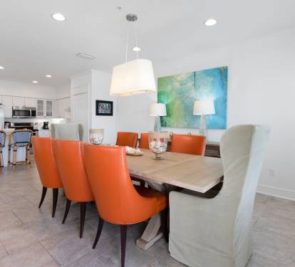 Gather around your spacious dining table where vibrant orange chairs and coastal artwork create the perfect setting for memorable meals together.