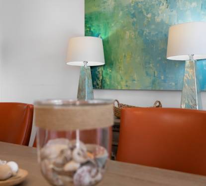 Gather around this stylish dining table where warm orange chairs and ocean-inspired artwork create the perfect setting for your memorable meals.