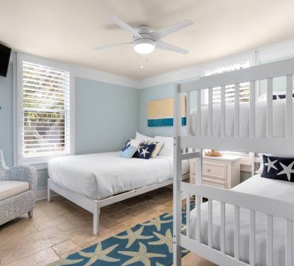 Your coastal-themed bedroom features crisp white bunk beds and nautical decor, creating a serene retreat where ocean breezes flow through plantation shutters.