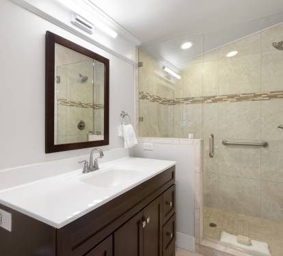 Your private bathroom features elegant white countertops, warm wood cabinetry, and a spacious glass-enclosed shower with beautiful tile details.
