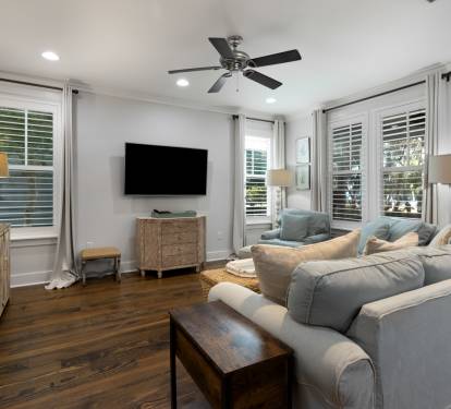 Sink into plush seating in your bright living space, where natural light flows through shuttered windows and coastal decor creates a serene retreat.