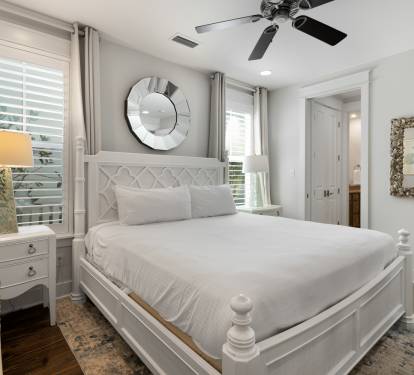 Drift off in your serene white bedroom with plush linens, coastal charm, and gentle ceiling fan keeping you cool.