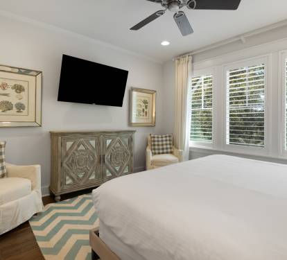 Relax in your peaceful bedroom with cozy seating, entertainment, and soft natural light streaming through plantation shutters.