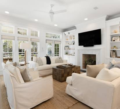 Sink into plush white sofas by the fireplace where natural light floods through elegant French doors, creating your perfect retreat.