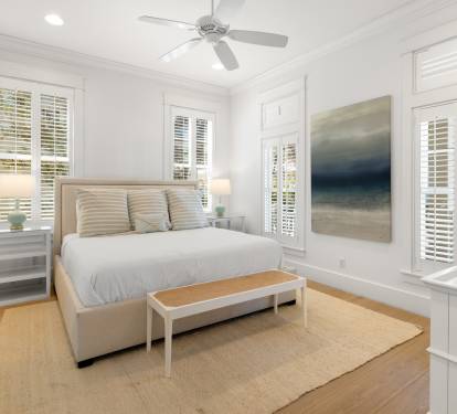 Unwind in your serene coastal bedroom with calming artwork and natural light streaming through shuttered windows.