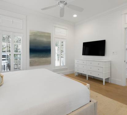 Unwind in your serene white bedroom featuring plush bedding, ocean-inspired artwork, and a wall-mounted TV for cozy nights in.