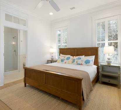 Your bright bedroom features warm wood furnishings and coastal-inspired linens, with natural light streaming through plantation shutters for peaceful mornings.