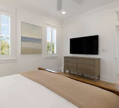 Relax in your bright, serene bedroom with crisp white linens, modern amenities, and peaceful garden views through plantation shutters.