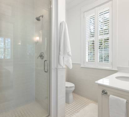 Step into your private spa-like bathroom with a luxurious glass shower, pristine white fixtures, and natural light streaming through plantation shutters.